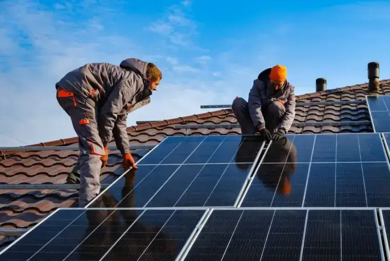 Zwei Arbeiter installieren Solarmodule auf einem Ziegeldach bei klarem Himmel für erneuerbare Energiegewinnung.