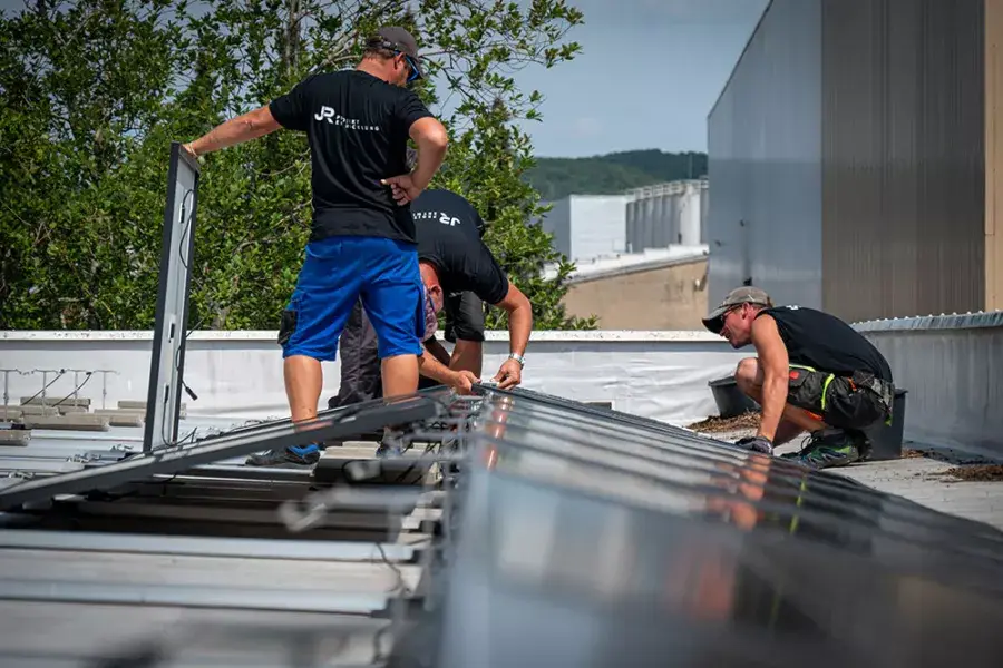 3 Arbeiter montieren eine Photovoltaikanlage auf einem Dach.