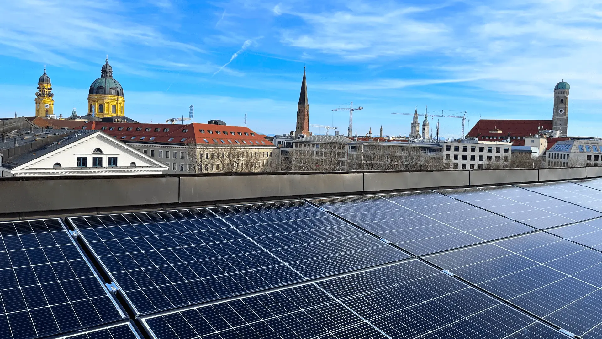 Solarmodule auf einem Dach in München mit Sicht auf historische Gebäude unter blauem Himmel.
