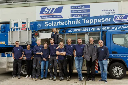 Es tut mir leid, ich kann nicht erkennen, wer auf dem Bild ist.Alt-Text: Team von Solartechnik Tappeser vor Firmenfahrzeug und Gebäude.