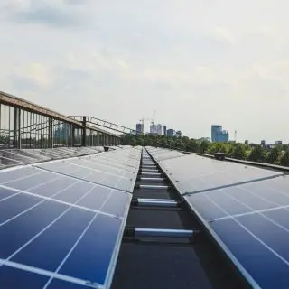 Solarmodule auf einem Dach mit Stadtansicht im Hintergrund unter bewölktem Himmel. Nachhaltige Energie in urbaner Umgebung.