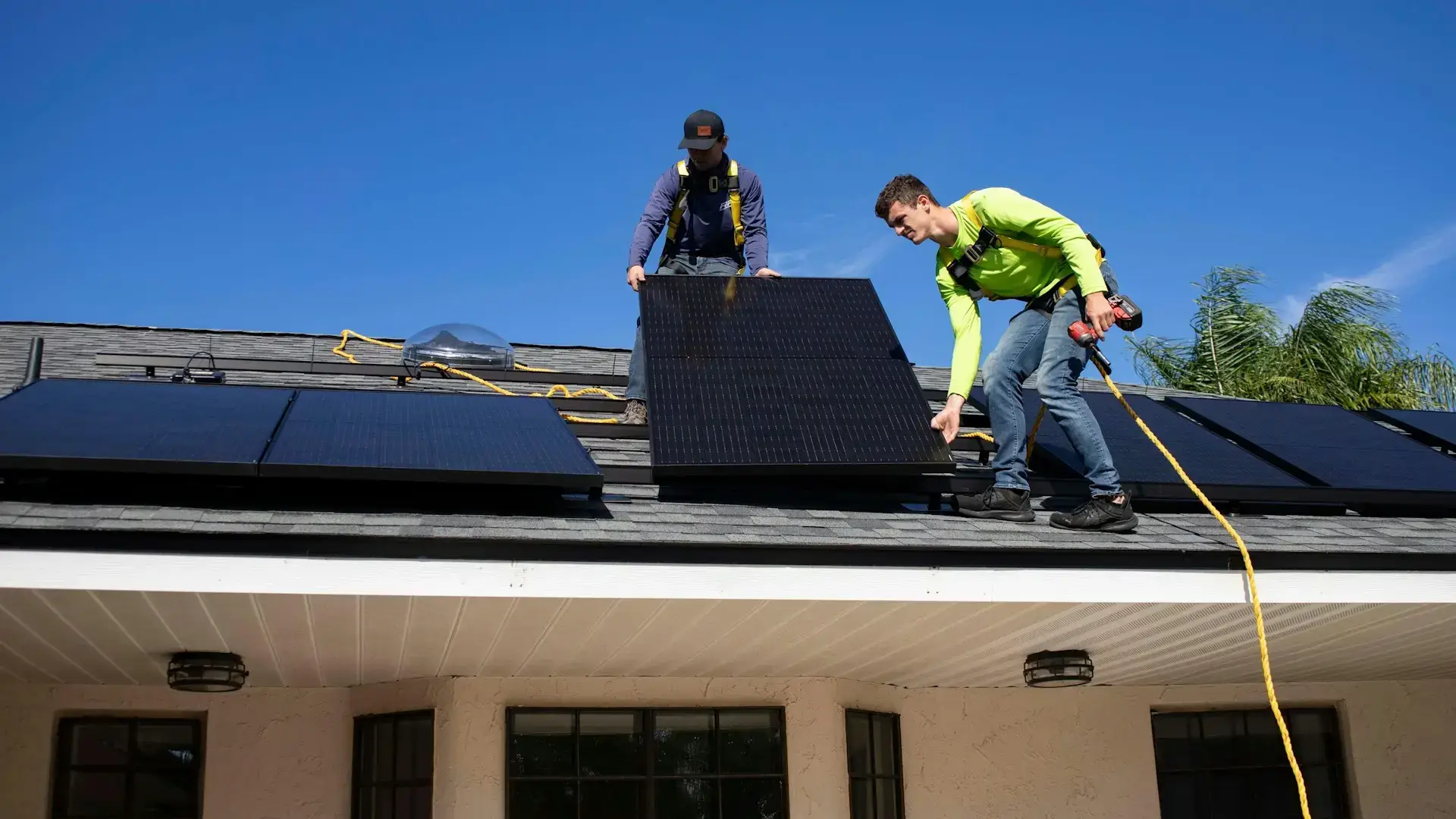 Techniker installieren Solarmodule auf einem Hausdach unter klarem blauem Himmel.
