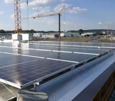 Solaranlagen auf einem Fabrikdach bei sonnigem Wetter mit Baukränen im Hintergrund.
