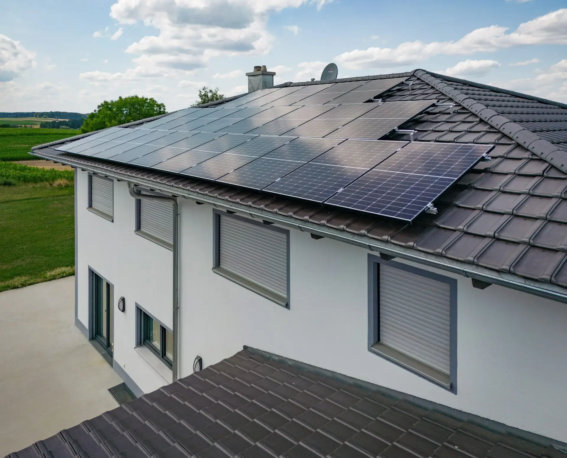 Hausdach mit installierten Solarpaneelen in ländlicher Umgebung unter blauem Himmel.