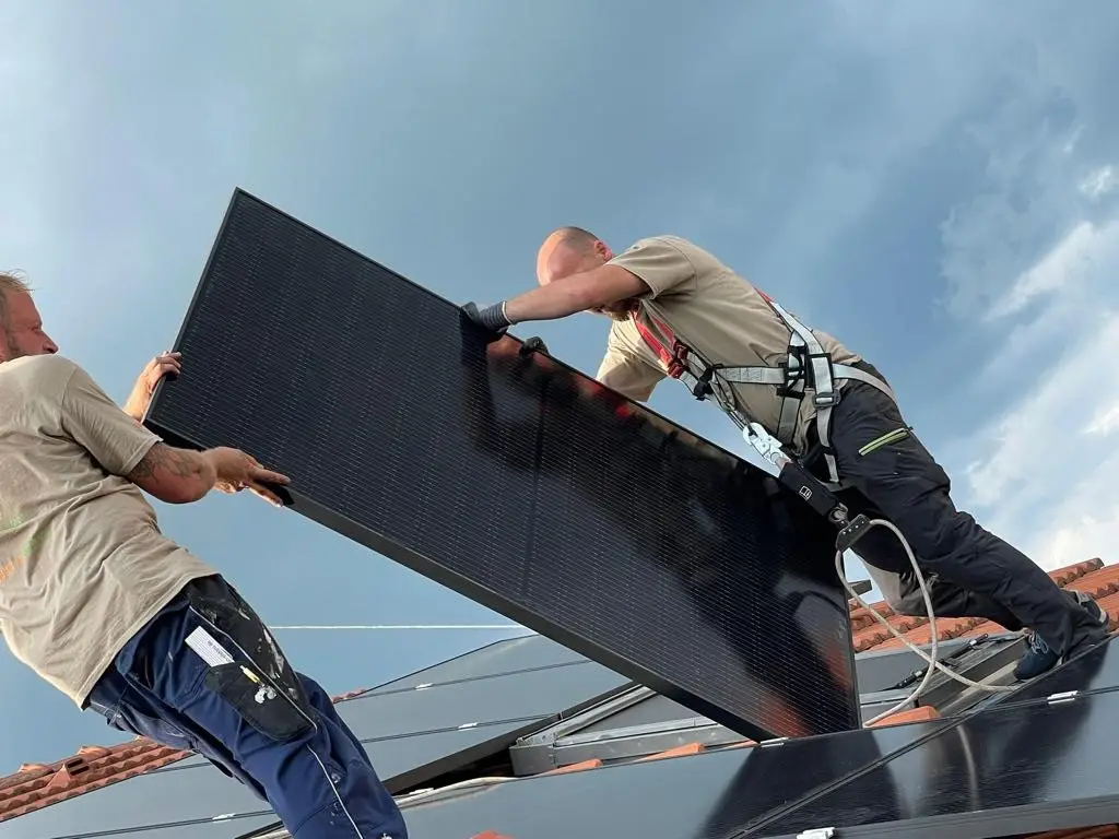 Zwei Arbeiter installieren Solarmodule auf einem Dach unter bewölktem Himmel, erneuerbare Energie in Deutschland.