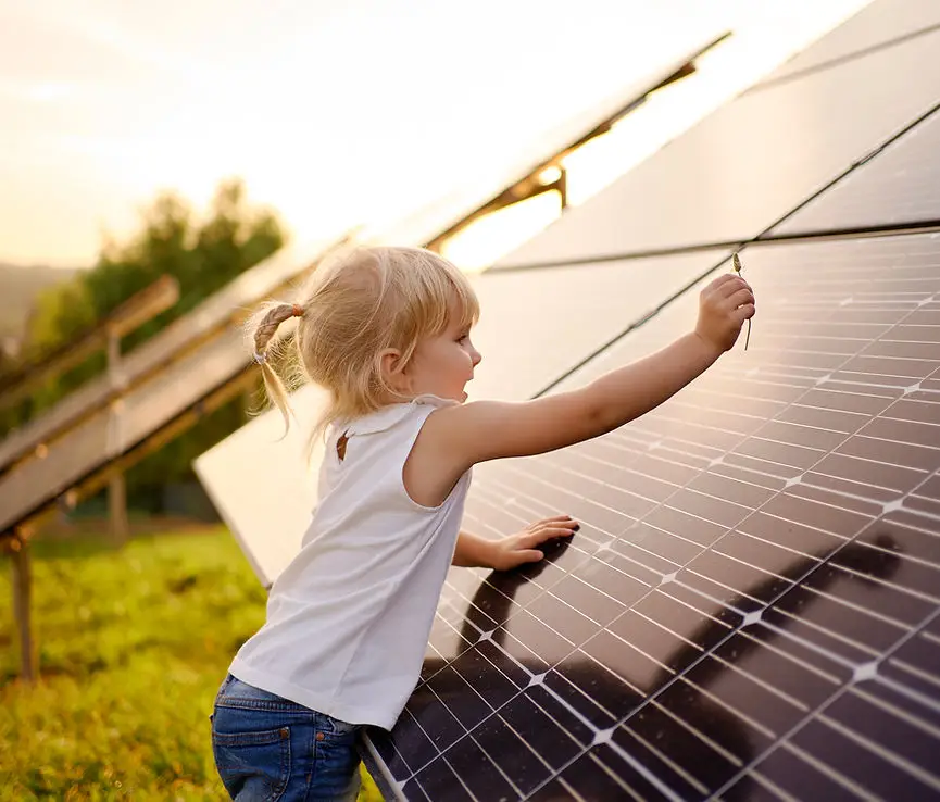 Mädchen reinigt Solarpanel auf Wiese bei Sonnenuntergang, erneuerbare Energie und Umweltbewusstsein in der Kindheit.