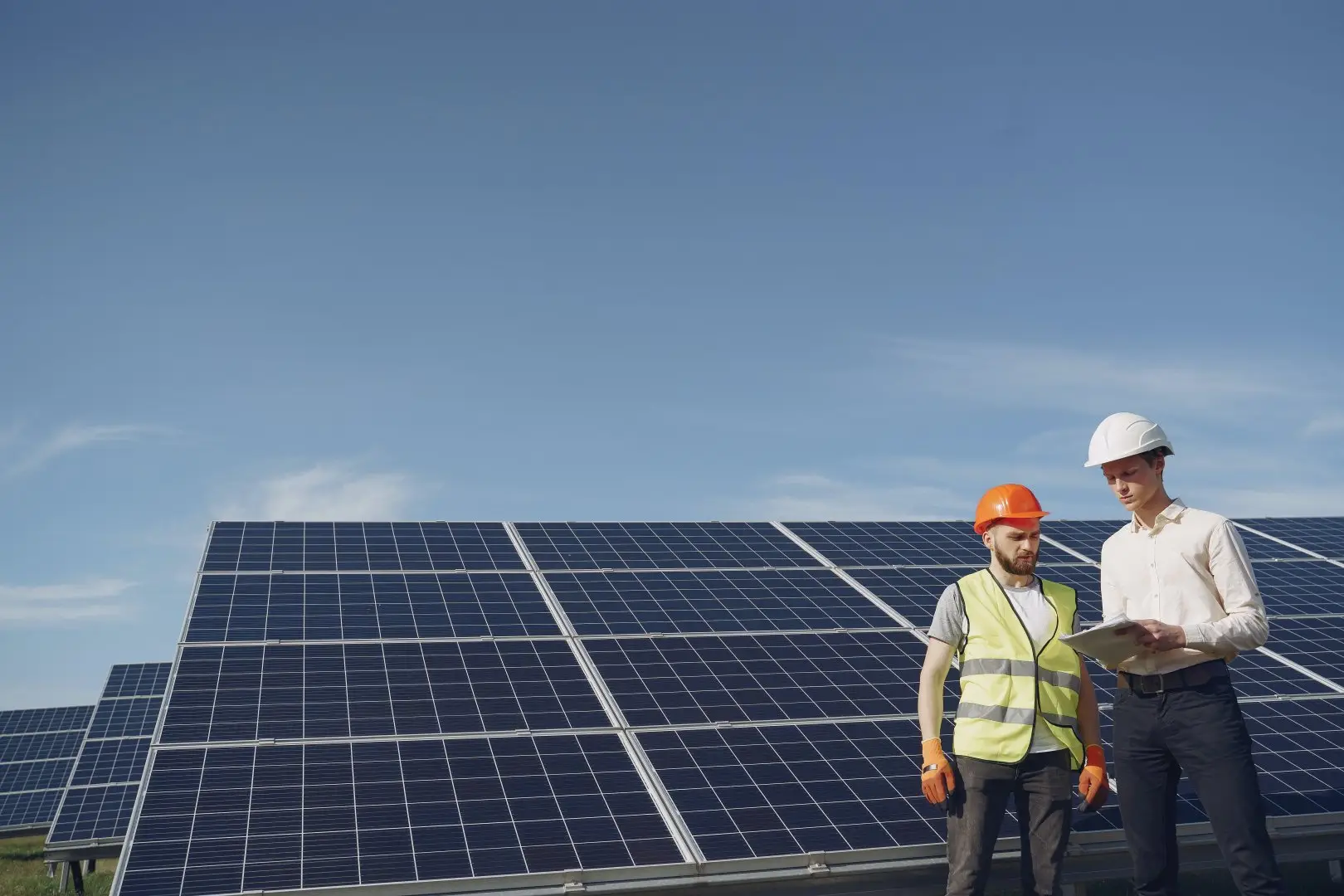 Zwei Ingenieure begutachten Solarmodule in einem Solarpark bei klarem Himmel.
