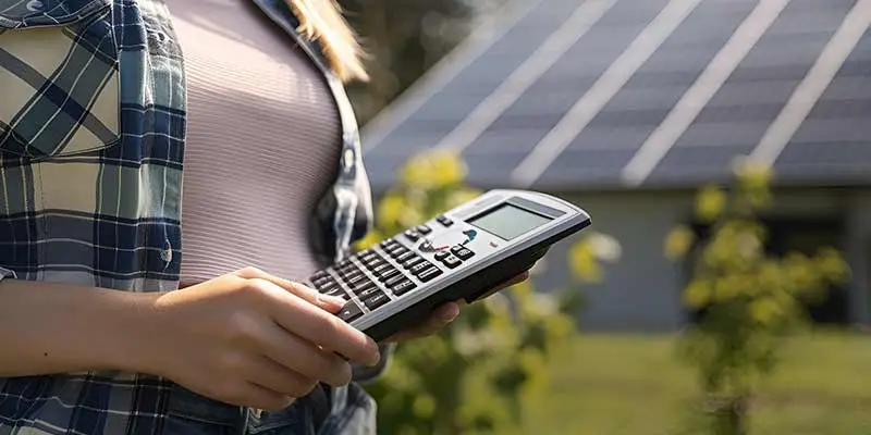 Frau hält einen Taschenrechner vor Solaranlage im Sonnenlicht, Symbol für erneuerbare Energien und Berechnungen.