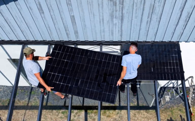 Zwei Personen installieren ein Solarpanel auf einem Dach bei klarem Himmel, nachhaltige Energieerzeugung.