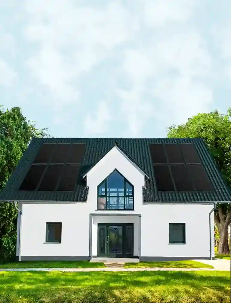 Modernes Einfamilienhaus mit Solarpanels auf dem Dach, umgeben von grünen Bäumen, blauer Himmel im Hintergrund.