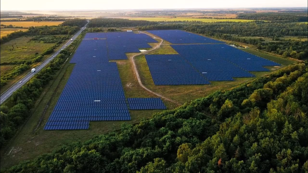 Große Solaranlage auf einem Feld, umgeben von Wäldern und Straßen, erneuerbare Energiequelle aus der Vogelperspektive.
