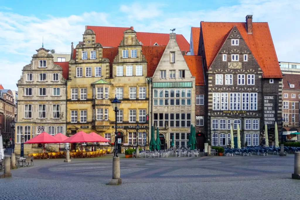 Historische Gebäude am Marktplatz in Bremen bei blauem Himmel, mit roten Dächern und leeren Tischen im Freien.
