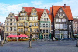 Historische Gebäude am Marktplatz in Bremen bei blauem Himmel, mit roten Dächern und leeren Tischen im Freien.
