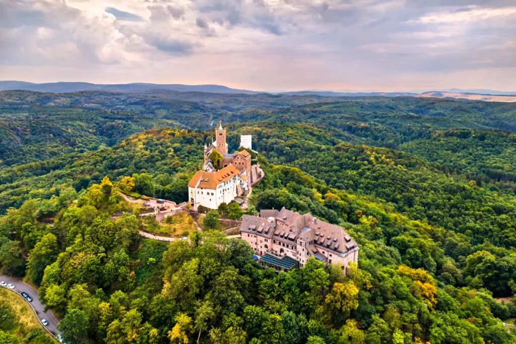 Luftaufnahme der Wartburg, umgeben von grünen Wäldern, unter bewölktem Himmel in Thüringen, Deutschland.