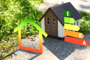 Miniaturhaus neben einem Energieeffizienz-Diagramm, das Energieklassen von A bis E zeigt, im Grünen.
