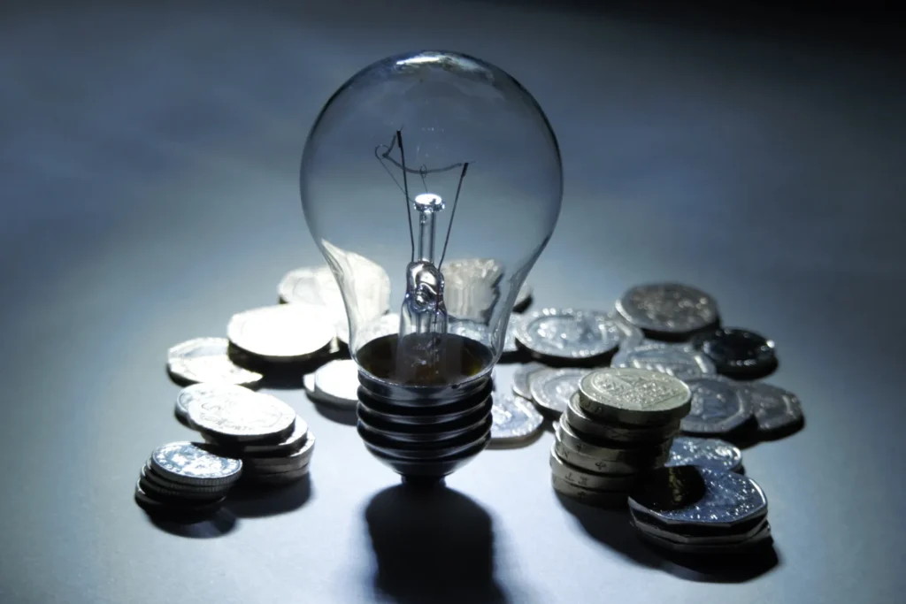 Glühbirne mit gestapelten Münzen symbolisiert Energieeinsparung und finanzielle Ersparnis im dunklen Hintergrund.