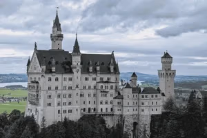 Schloss Neuschwanstein in Bayern, Deutschland, umgeben von grüner Landschaft und unter dramatischem Himmel.